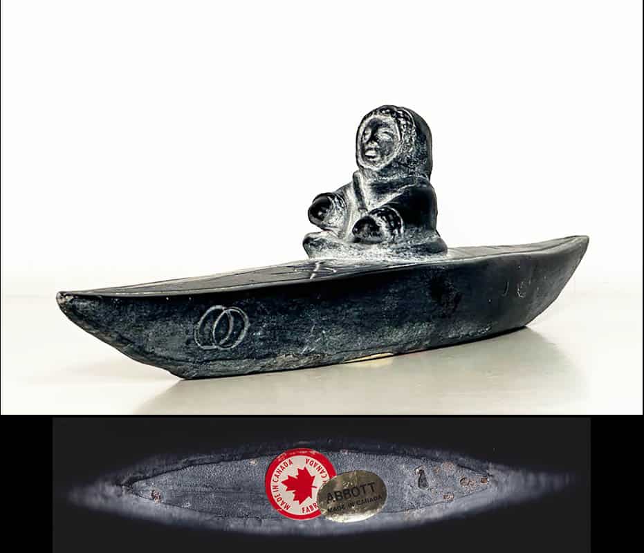 [Grönland ; Skulptur] : SKULPTUR, täljsten, inuitbarn i kajak. Formgjuten i ett täljstensliknande (soapstone) material (turistsouvenir från andra hälften av 1900-talet)