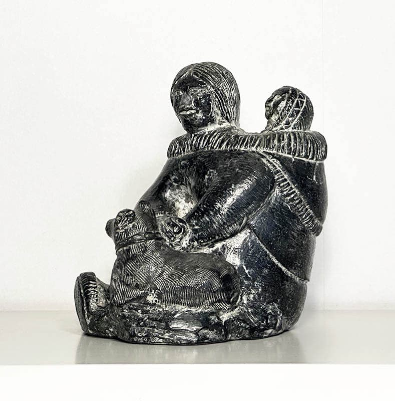 [Grönland ; Skulptur] : SKULPTUR, täljsten, inuitkvinna med barn på ryggen och vilande hund. Formgjuten i ett täljstensliknande (soapstone) material (turistsouvenir från andra hälften av 1900-talet)